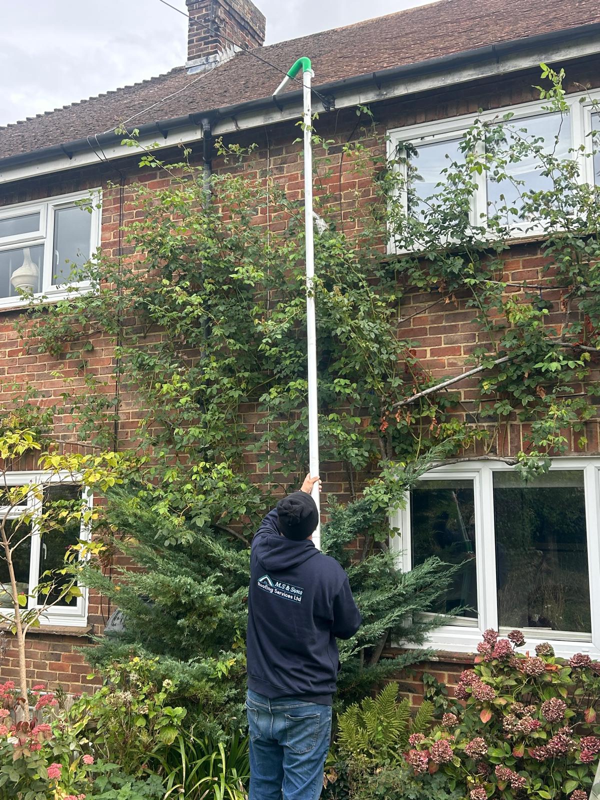M.S & Sons team clearing gutters from the ground with a reach pole